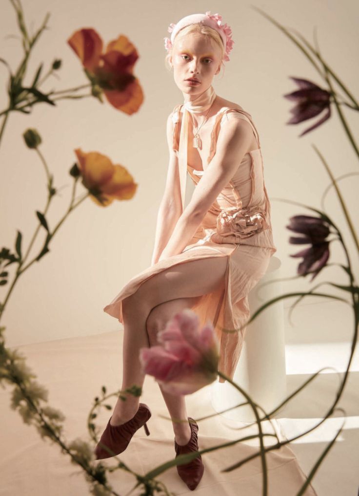 a woman sitting on top of a white table next to flowers