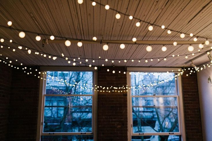 string lights are hanging from the ceiling in front of two windows with snow covered trees outside