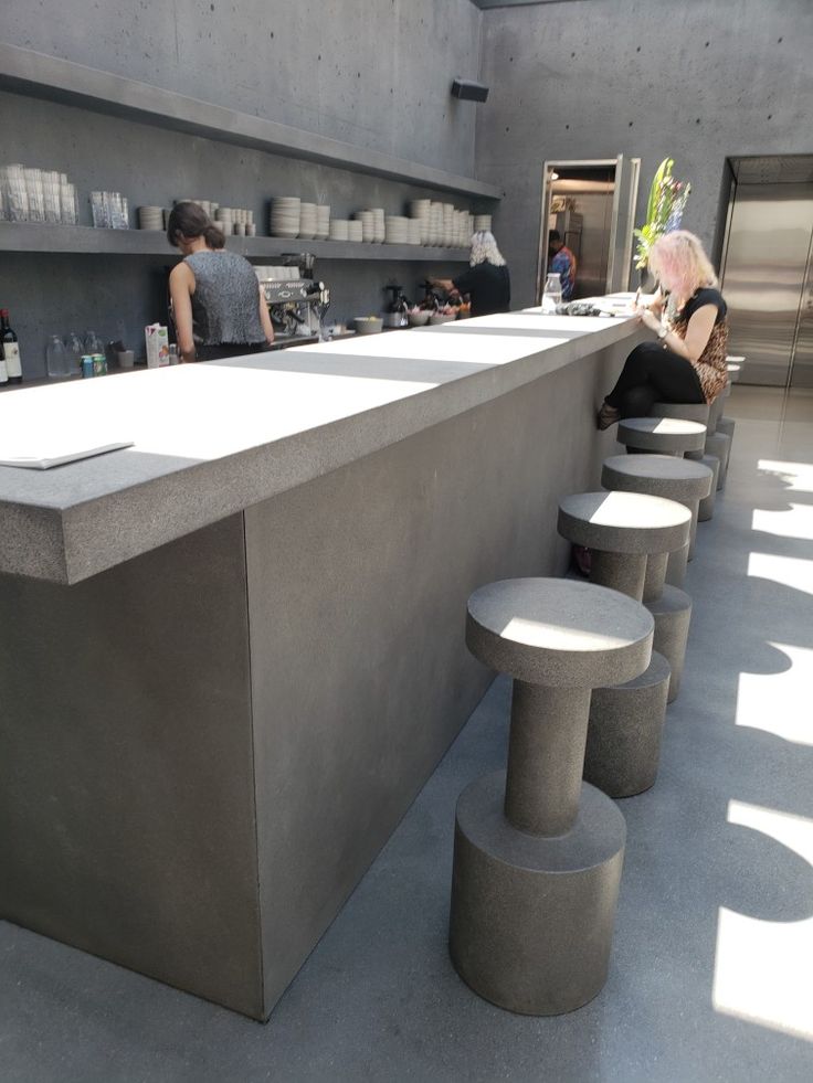 people are standing at the counter in an open space with concrete counters and stools