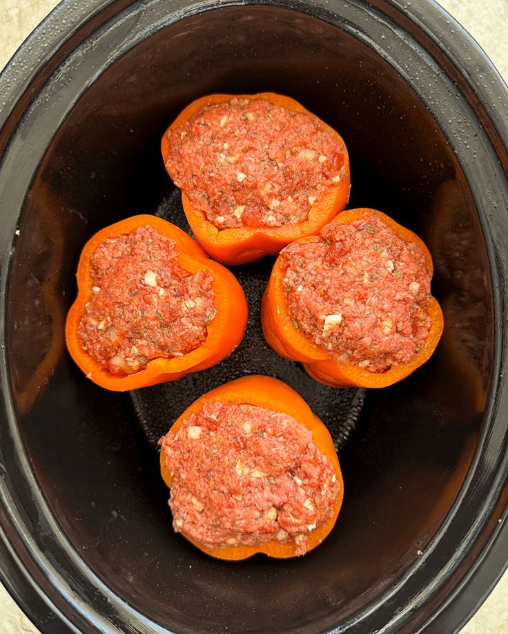 four stuffed peppers in an air fryer with meat toppings on the top and bottom