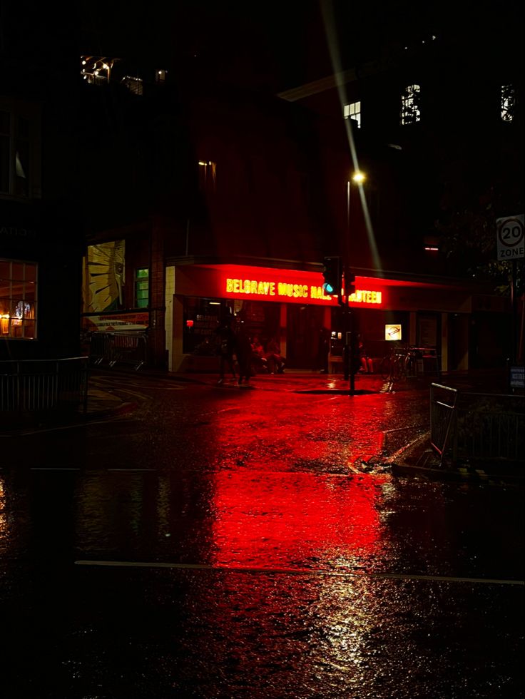 a red traffic light sitting on the side of a wet road at night with buildings in the background