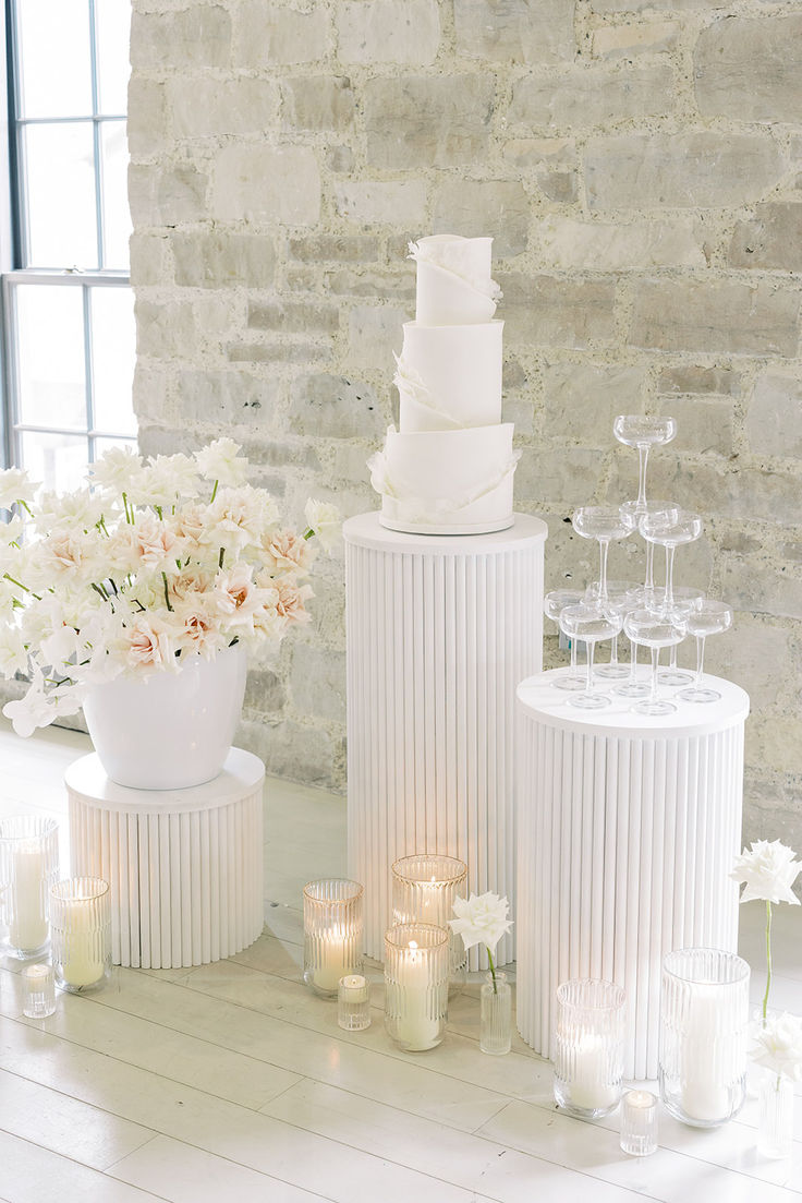 a white wedding cake sitting on top of a table next to vases filled with flowers