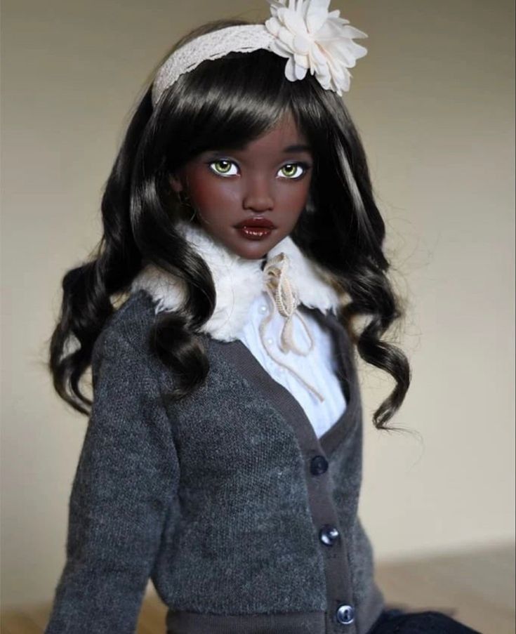 a doll with long black hair wearing a gray sweater and white flower in her hair