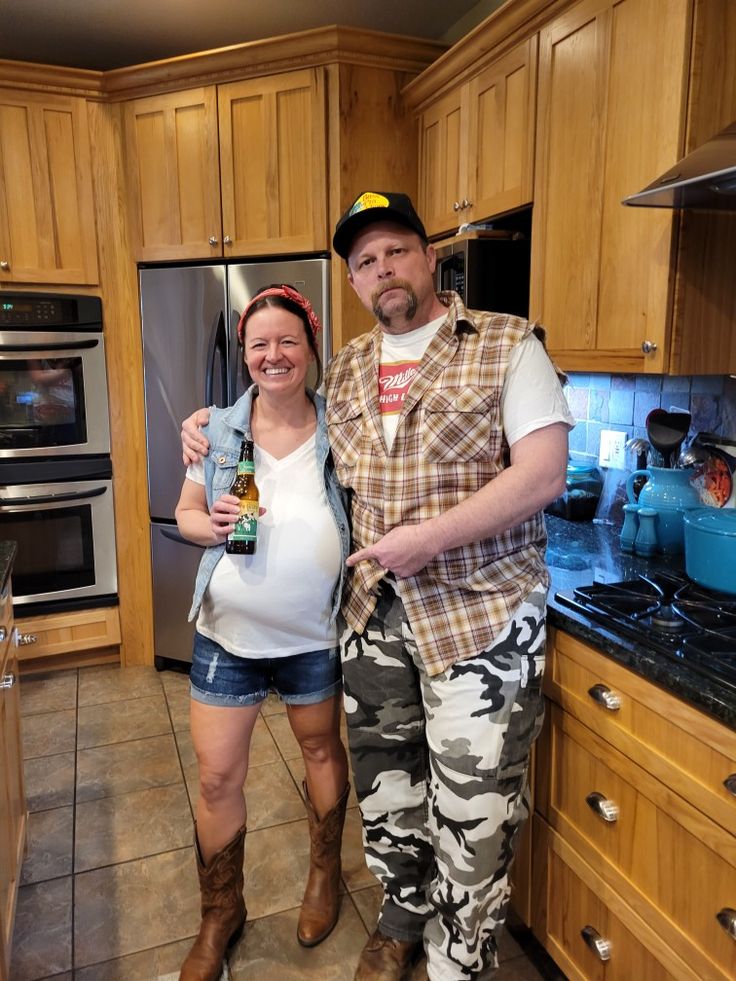 a man and woman standing in a kitchen holding cans of beer, smiling at the camera