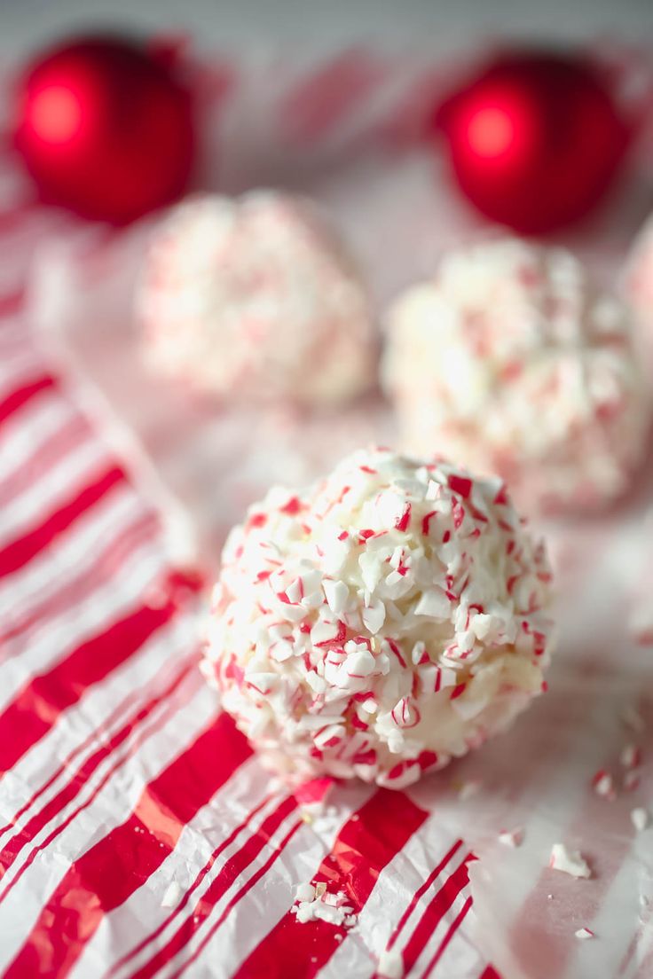 some white and red candy balls are on a striped tablecloth with christmas ornaments in the background