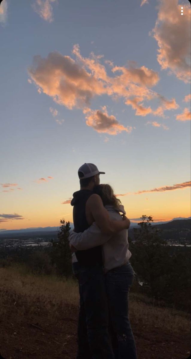 a man and woman embracing each other while the sun is setting in the sky behind them