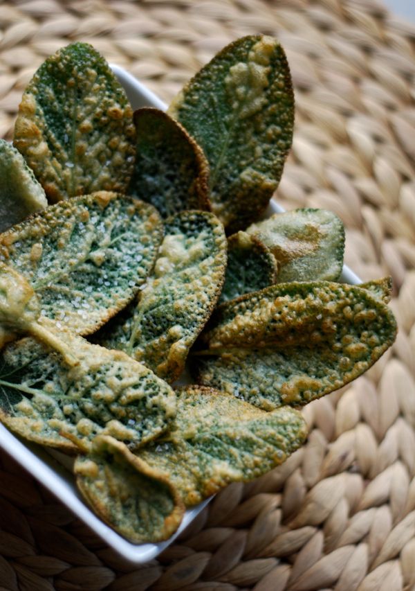 a bowl filled with green leaves on top of a wicker tablecloth next to a woven basket