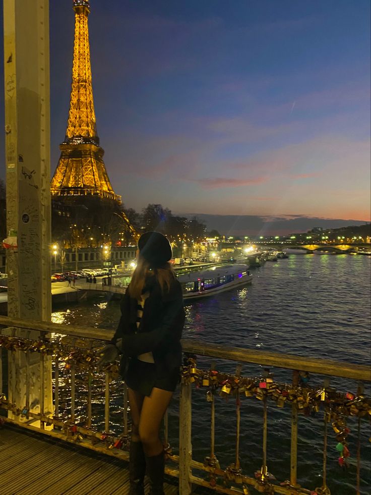 a woman standing on top of a bridge next to the eiffel tower at night