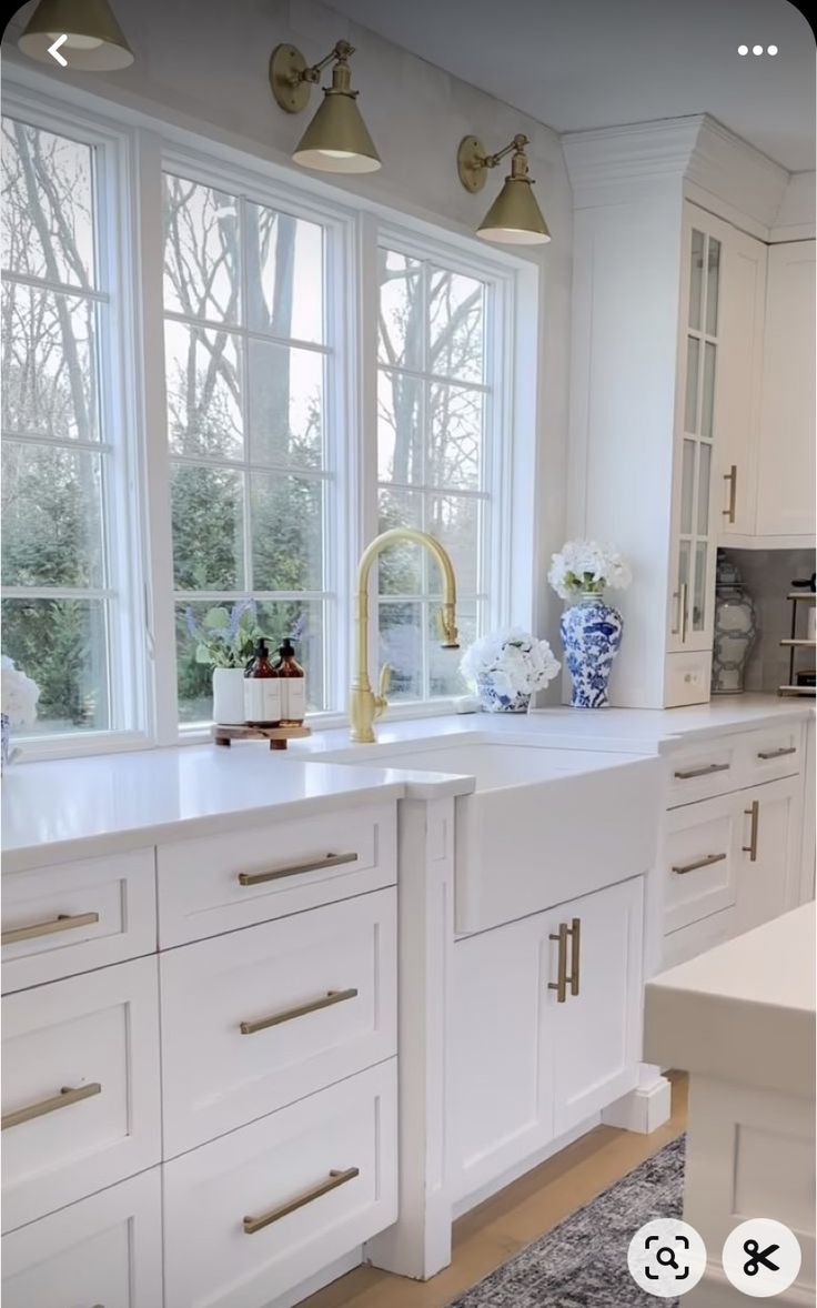 a kitchen with white cabinets and gold faucet lights in the window sill