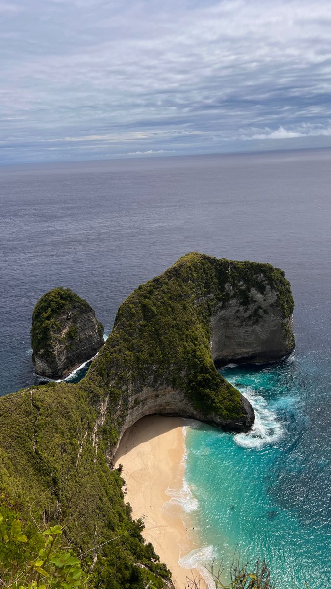 two large rocks sticking out of the ocean next to a sandy beach with blue water