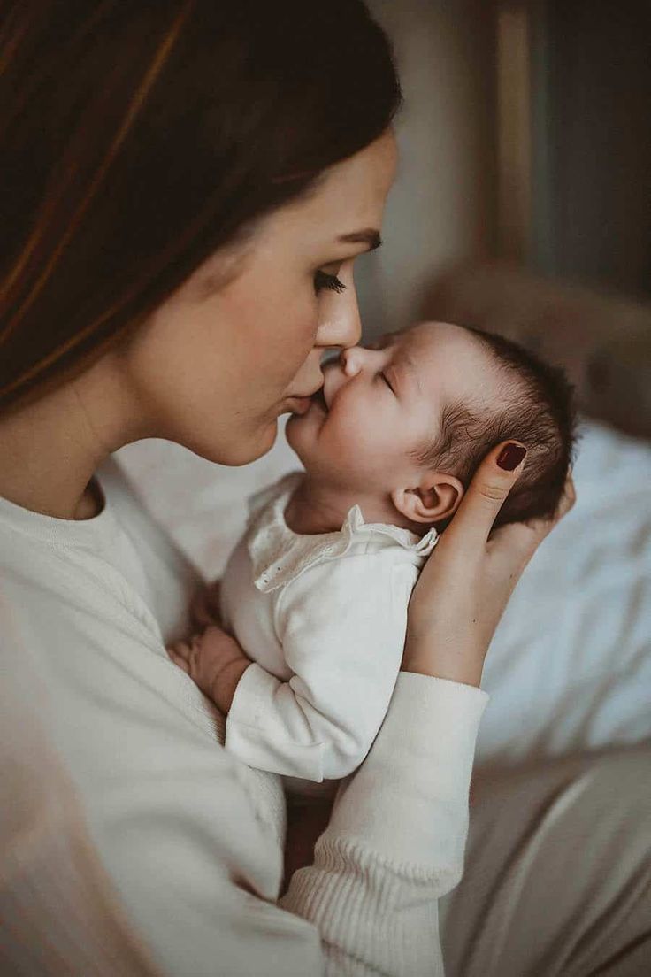 a woman holding a baby in her arms and kissing it's face with both hands