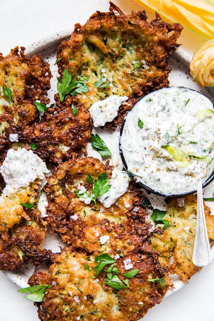 a plate topped with fried food next to a bowl of ranch dressing and a spoon