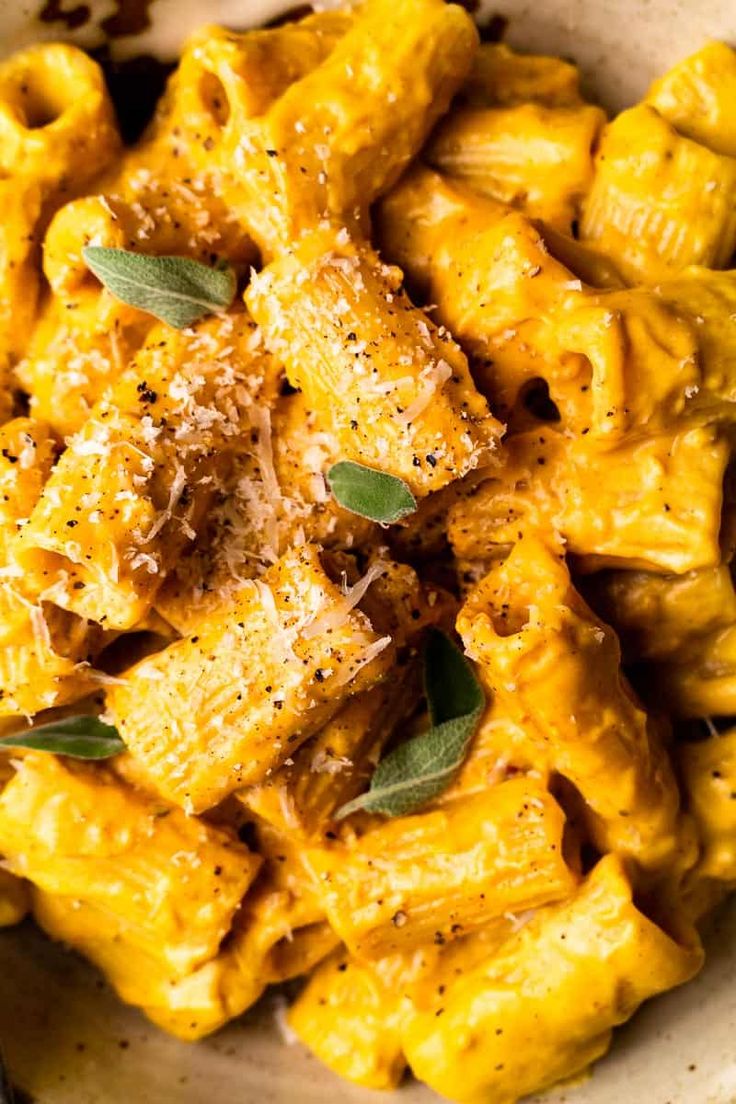 a white bowl filled with pasta covered in cheese and sage leaf sprinkled on top