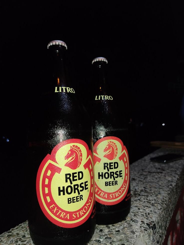 two red horse beer bottles sitting on top of a stone wall in front of a dark background