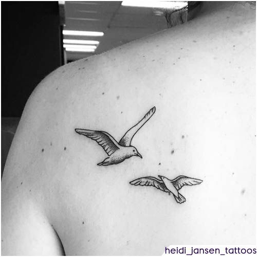 the back of a woman's shoulder with two seagulls flying above it