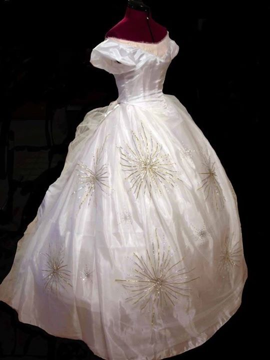 a white dress with gold stars is on display in a black background and it has a mannequin behind it