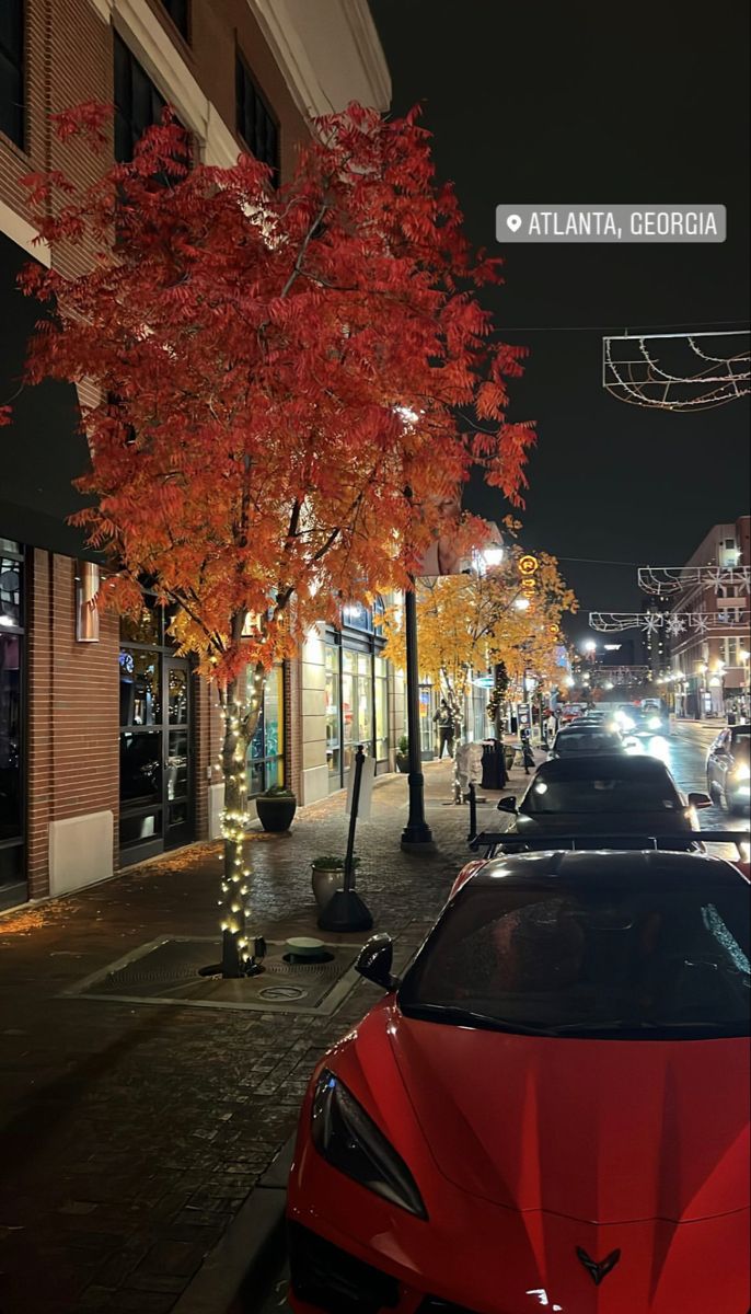 a red car parked on the side of a street next to a tree with orange leaves