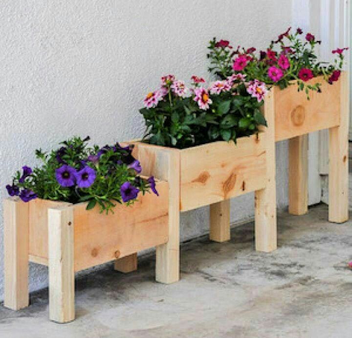 three wooden planters with purple and pink flowers in them sitting on the ground next to a wall