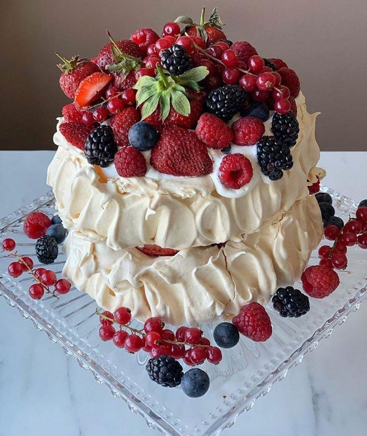 a cake with berries, raspberries and cream frosting on a glass platter