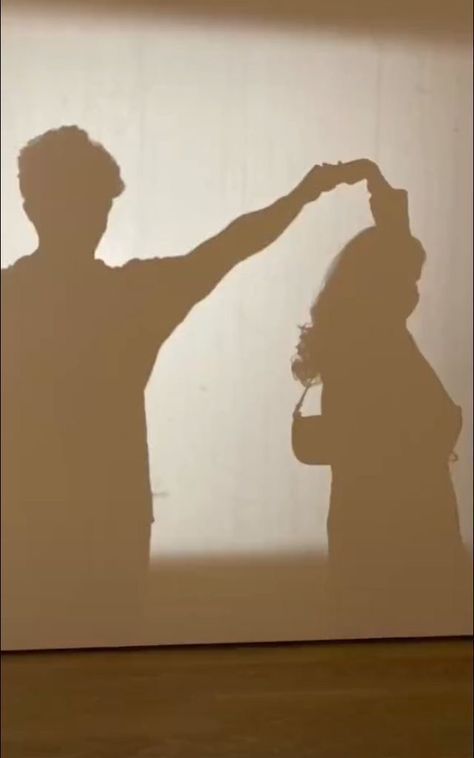 two people standing in front of a wall with their shadow on the wall behind them