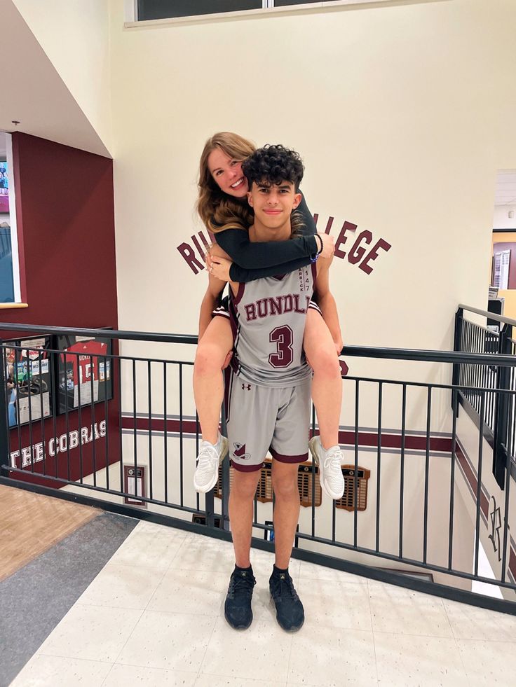 a boy and girl are holding each other in the middle of a hallway with railings