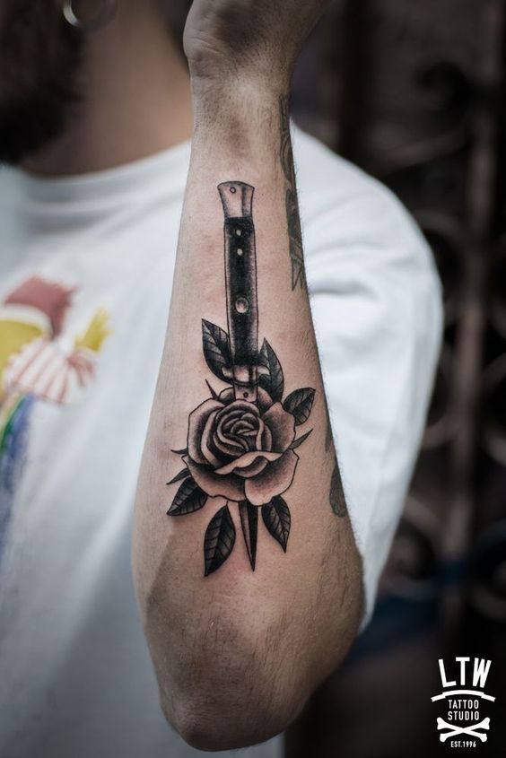 a man's arm with a rose and knife tattoo on the left side of his arm