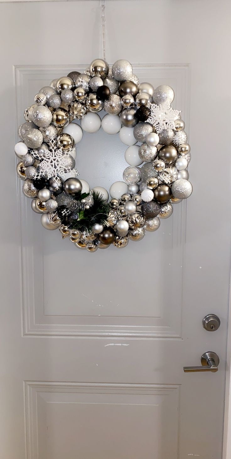 a christmas ornament wreath hanging on the front door with silver and white ornaments