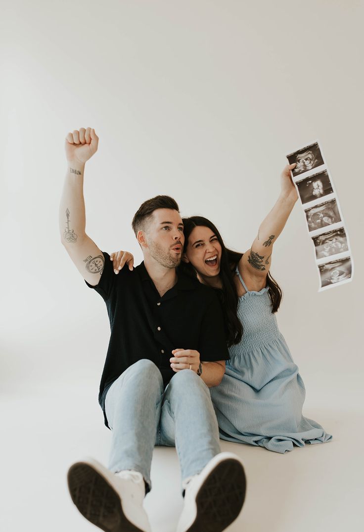 a man and woman sitting on the ground with their arms in the air holding up photos