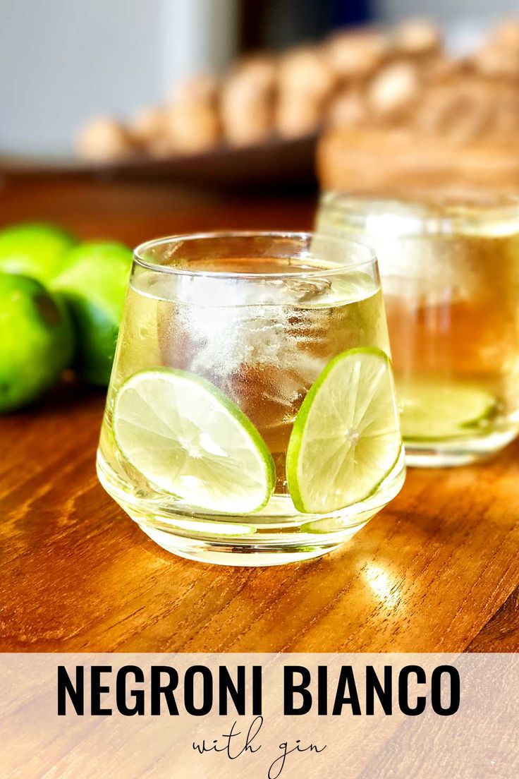 two glasses filled with lemonade and limes on top of a wooden table