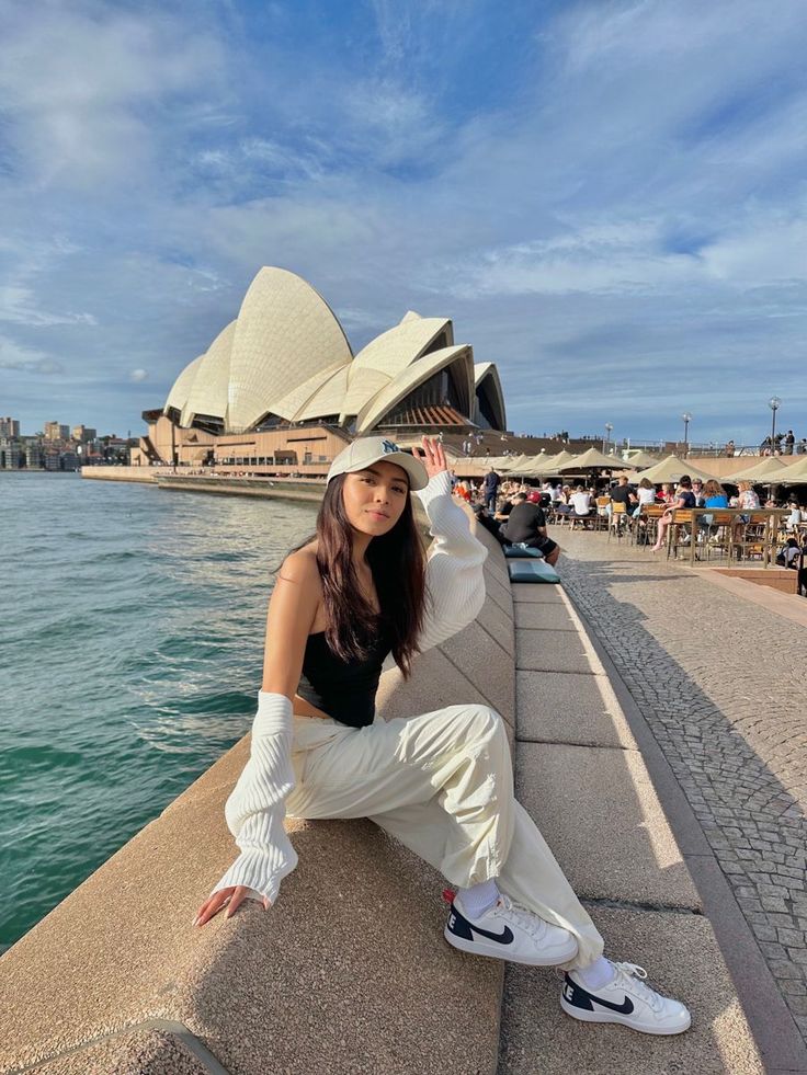 a woman posing for a photo in front of the sydney opera house with her hat on