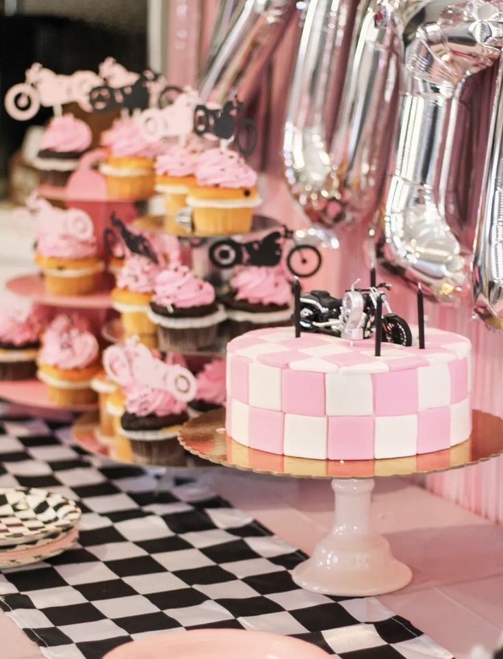 a table topped with lots of pink and black cupcakes