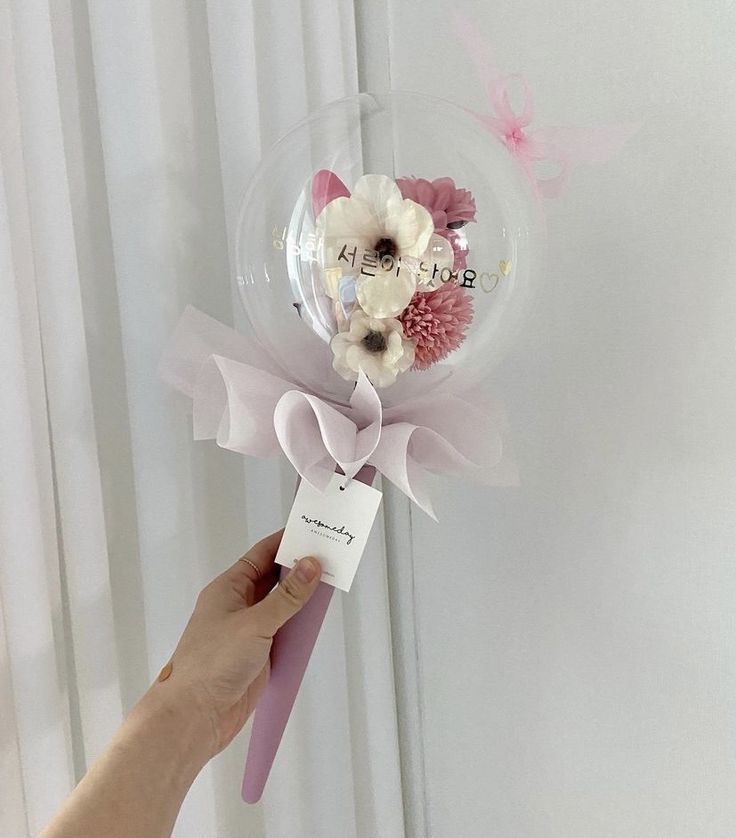 a person holding a pink and white flower in a clear bubble with a name tag