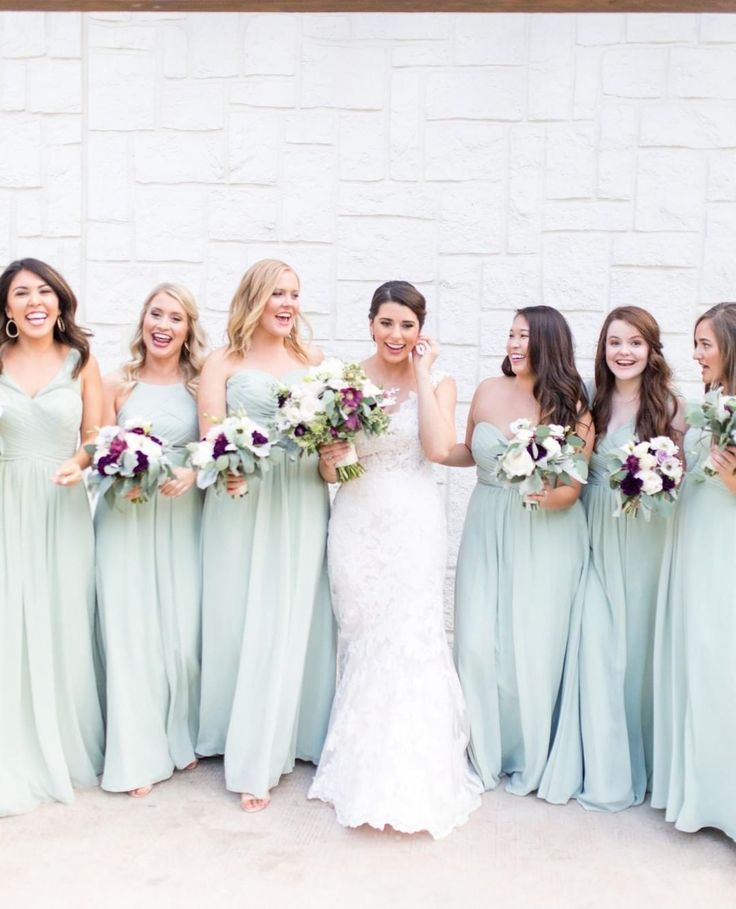 a group of women standing next to each other wearing dresses and holding bouquets in their hands