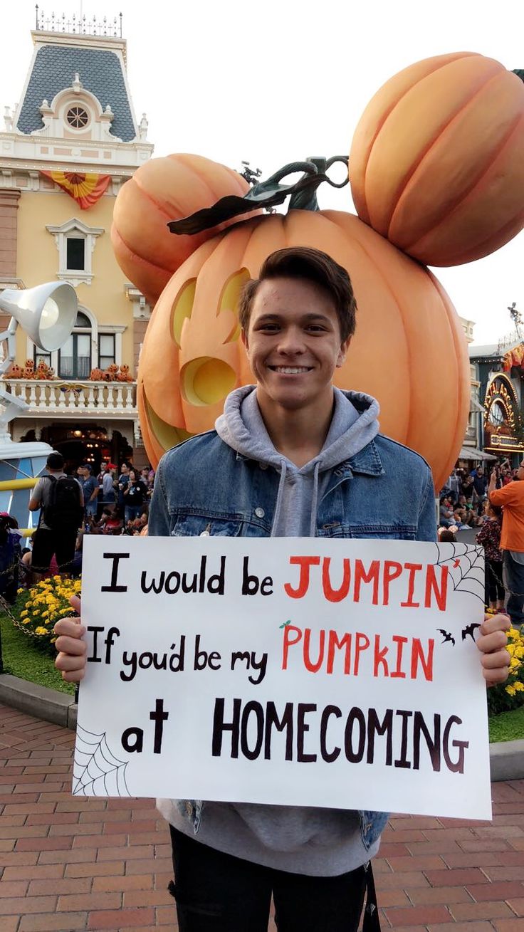 a man holding up a sign in front of mickey mouse's pumpkin head at disneyland