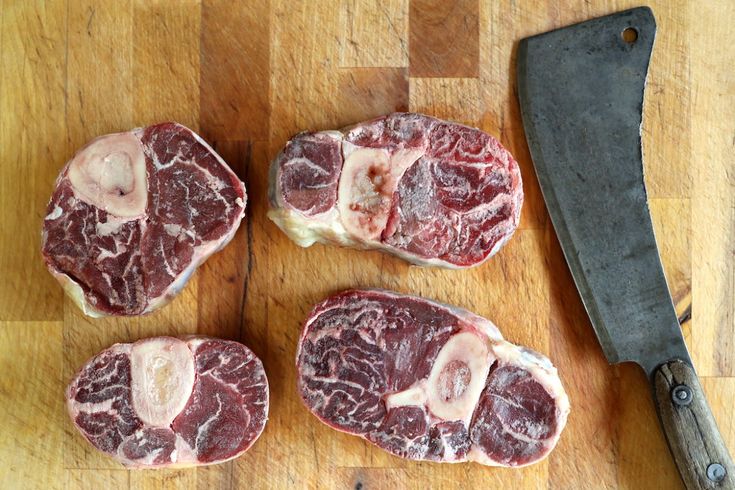 four pieces of raw meat sitting on top of a wooden cutting board next to a knife