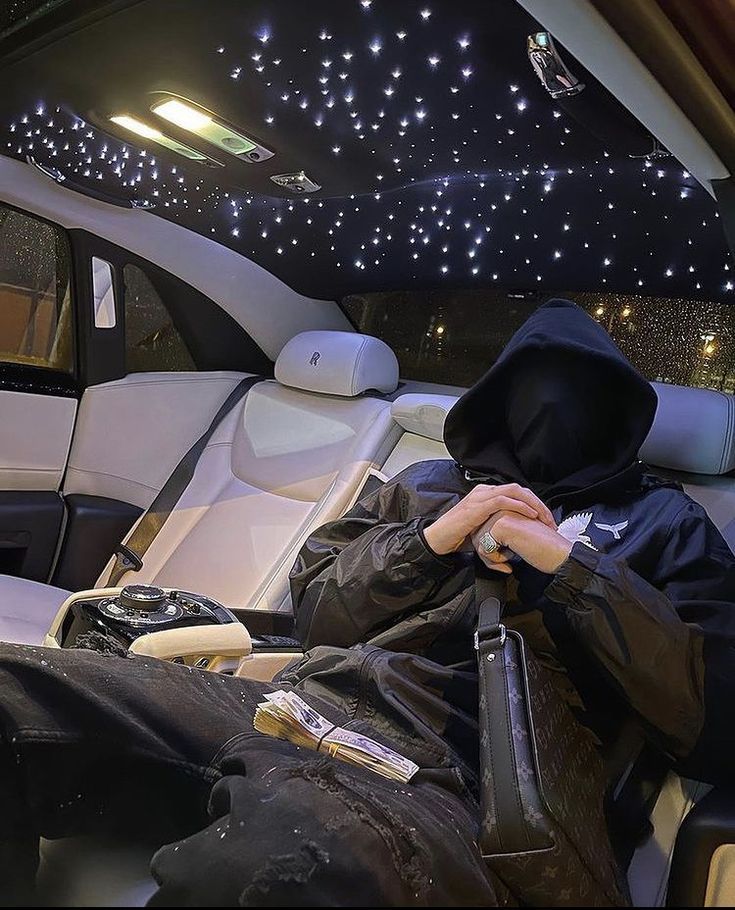 a person sitting in the back seat of a car wearing a hoodie and black pants