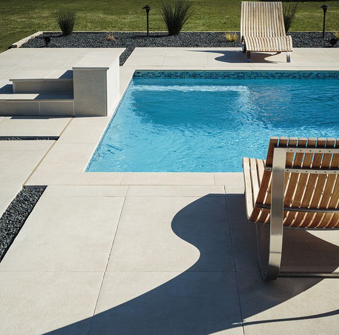 an empty swimming pool with two wooden chairs next to it and grass in the background