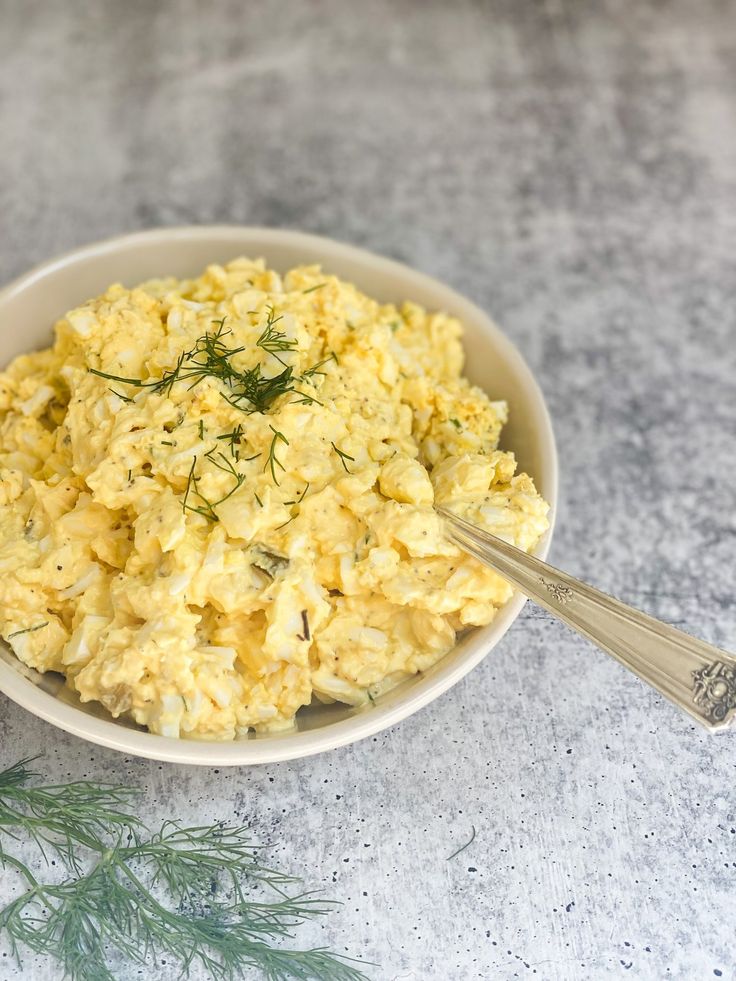 a white bowl filled with scrambled eggs on top of a gray counter next to a green plant