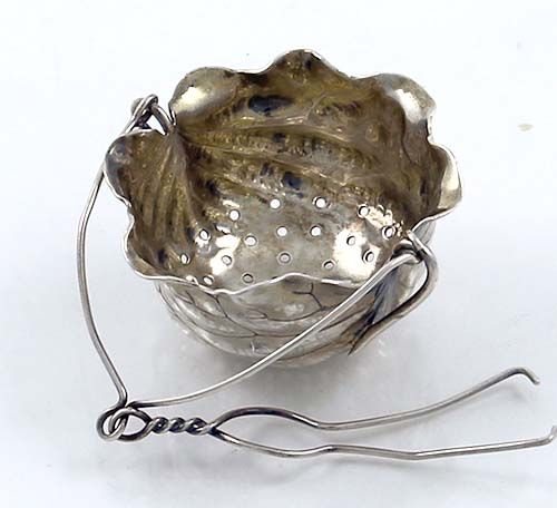 a metal bowl sitting on top of a white table next to a pair of tongs