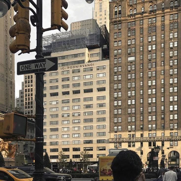 people are walking on the street in front of tall buildings and traffic lights with one way signs