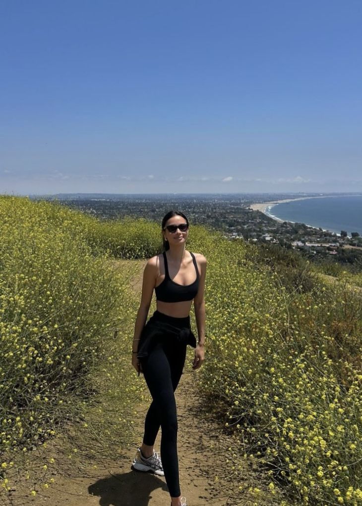 a woman is walking down a trail near the ocean and yellow wildflowers on a sunny day