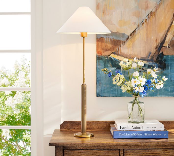 a vase with flowers on top of a wooden table next to a lamp and books