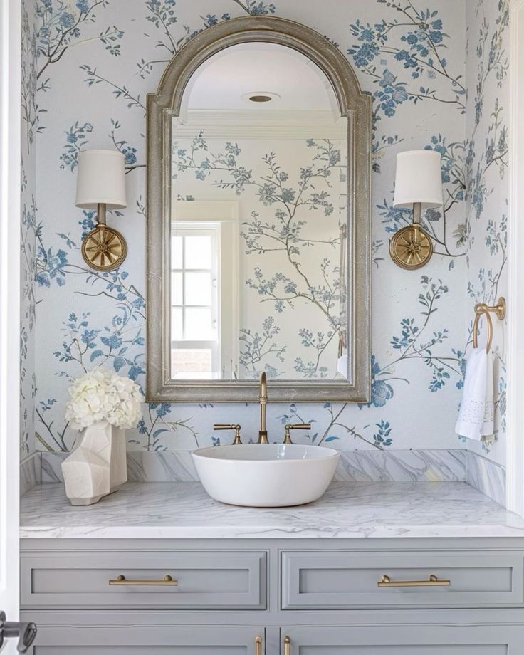 a bathroom with blue and white wallpaper, gold fixtures and a round mirror above the sink