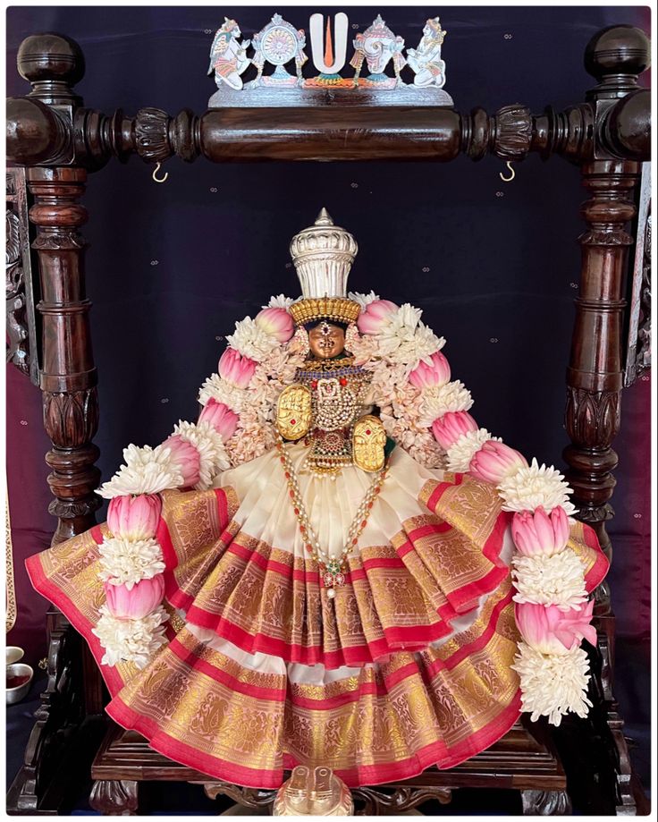 an idol is displayed in front of a wooden frame with flowers on the sides and a crown above it