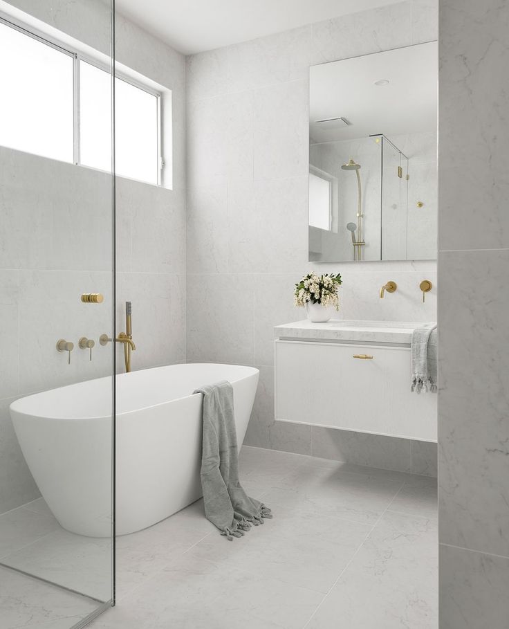 a white bathtub sitting next to a bathroom sink under a mirror in a bathroom