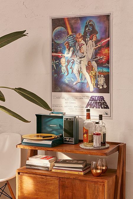 a star wars poster hangs on the wall next to a wooden table with books and drinks