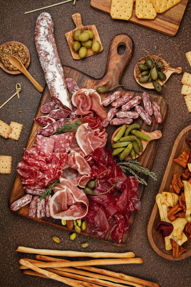 an assortment of meats and cheeses on a cutting board with breadsticks