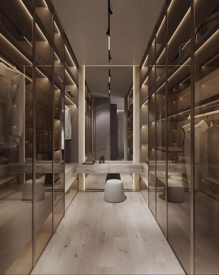 a large walk in closet with glass walls and wooden flooring, lighted by recessed lights