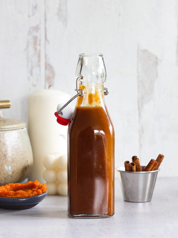 a glass bottle filled with caramel sauce next to some cinnamons and other ingredients