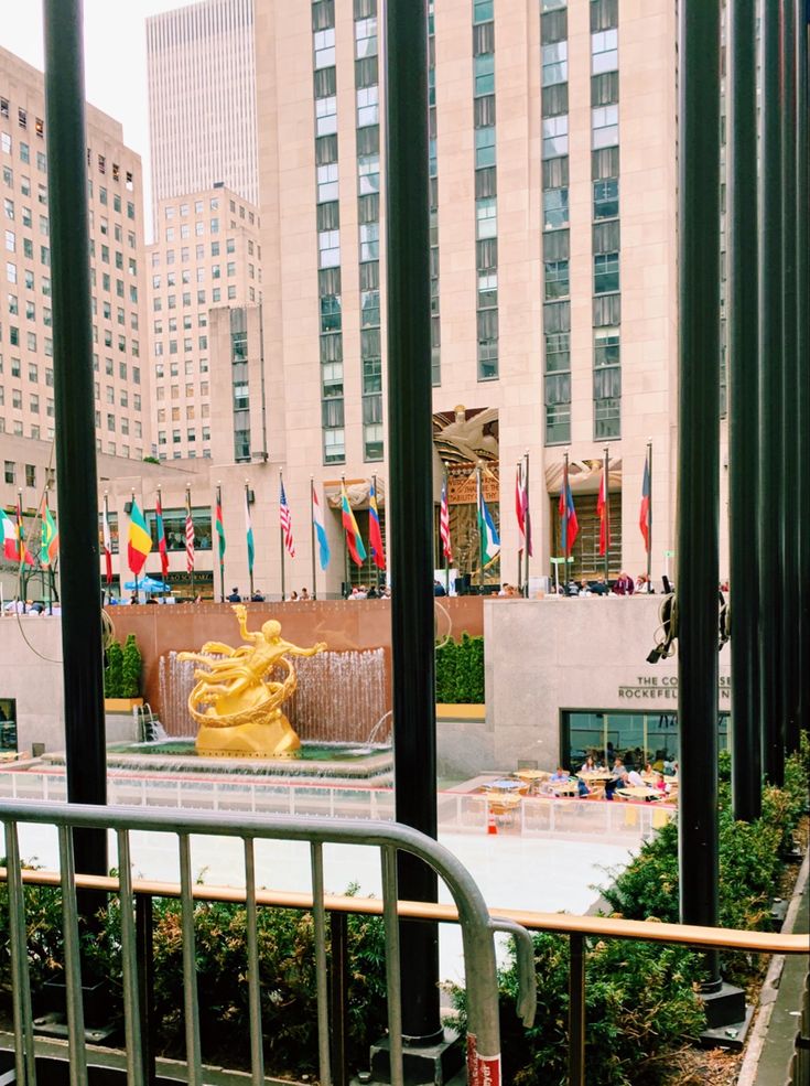 a large yellow statue sitting in the middle of a city park next to tall buildings